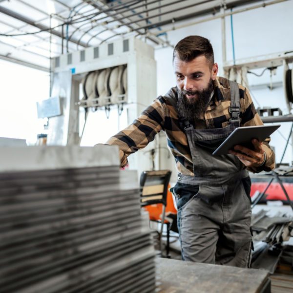 A man in overalls, holding a tablet in one hand, and counting steel sheets